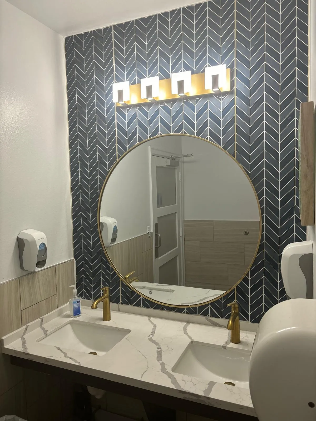 Remodeled bathroom with navy chevron tile, round gold mirror and marble vanity