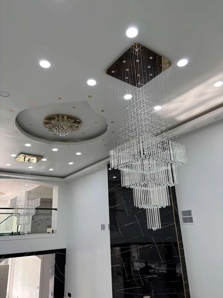 Cascading crystal chandelier with gold ceiling panel and marble accent wall