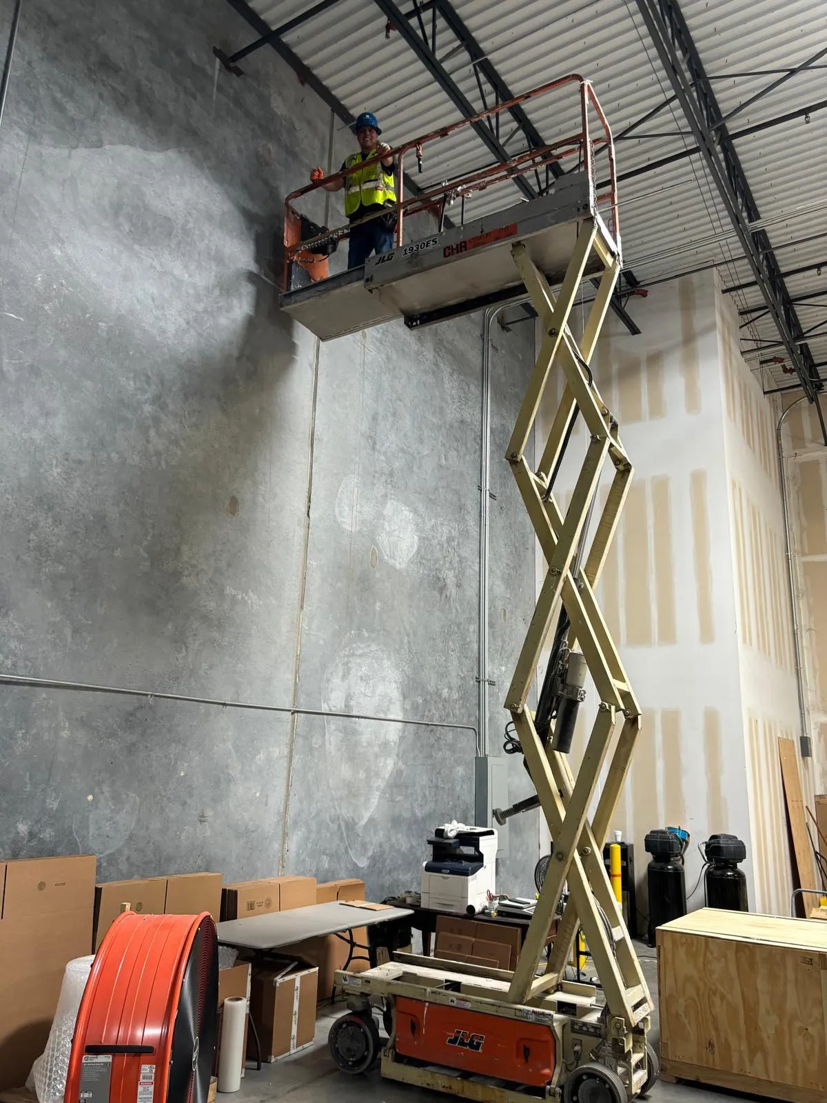 Technician in hi-vis gear on a scissor lift in a commercial warehouse